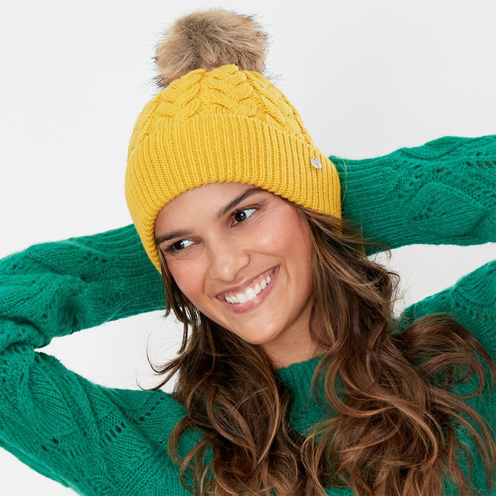 Gorro con pompón Elena punto de cable Pompón de piel sintética de Joules - Mostaza
