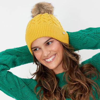 Gorro con pompón Elena punto de cable Pompón de piel sintética de Joules - Mostaza